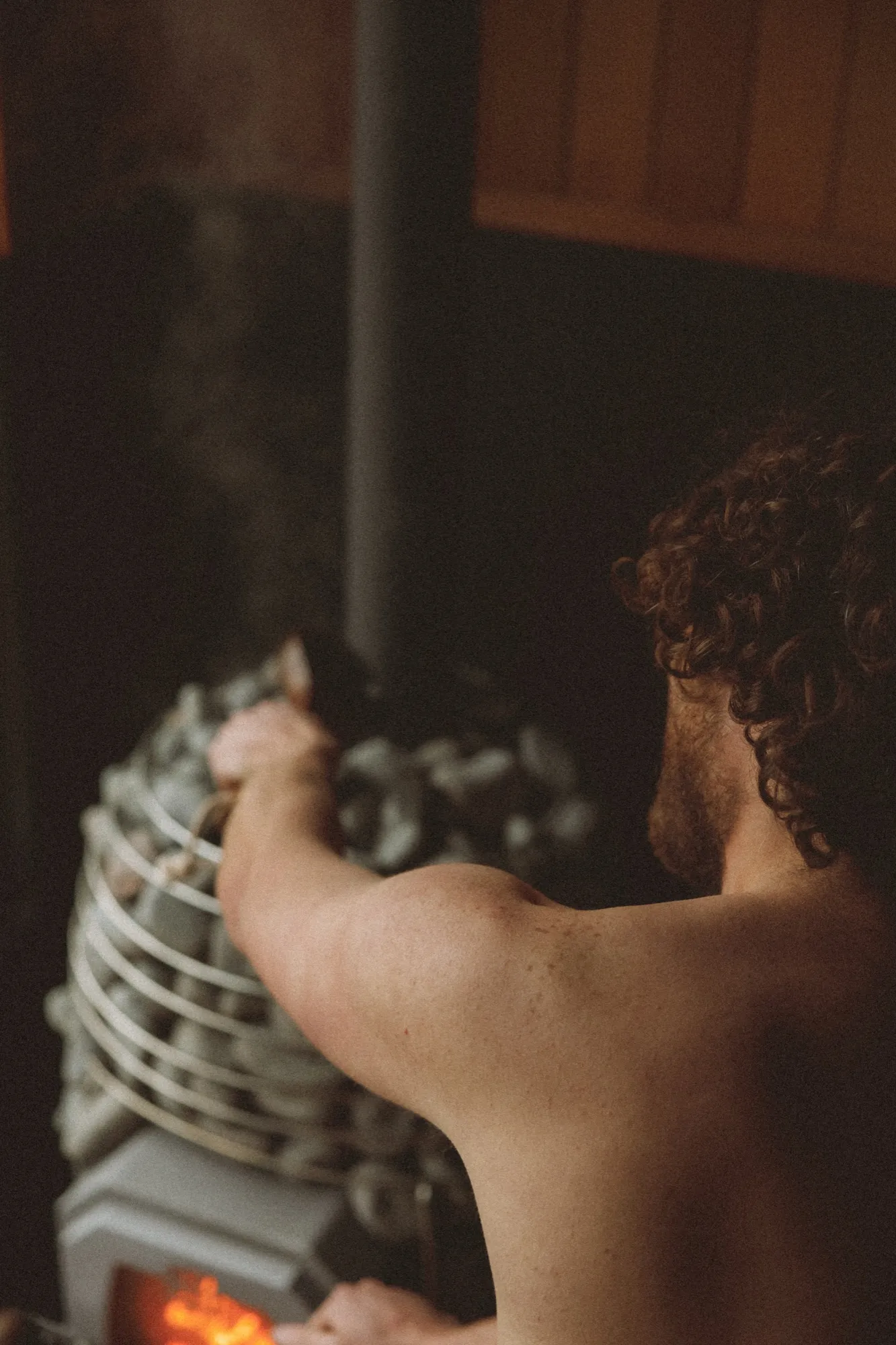 A bather ladling water onto the hot stones of a wood-fired sauna heater