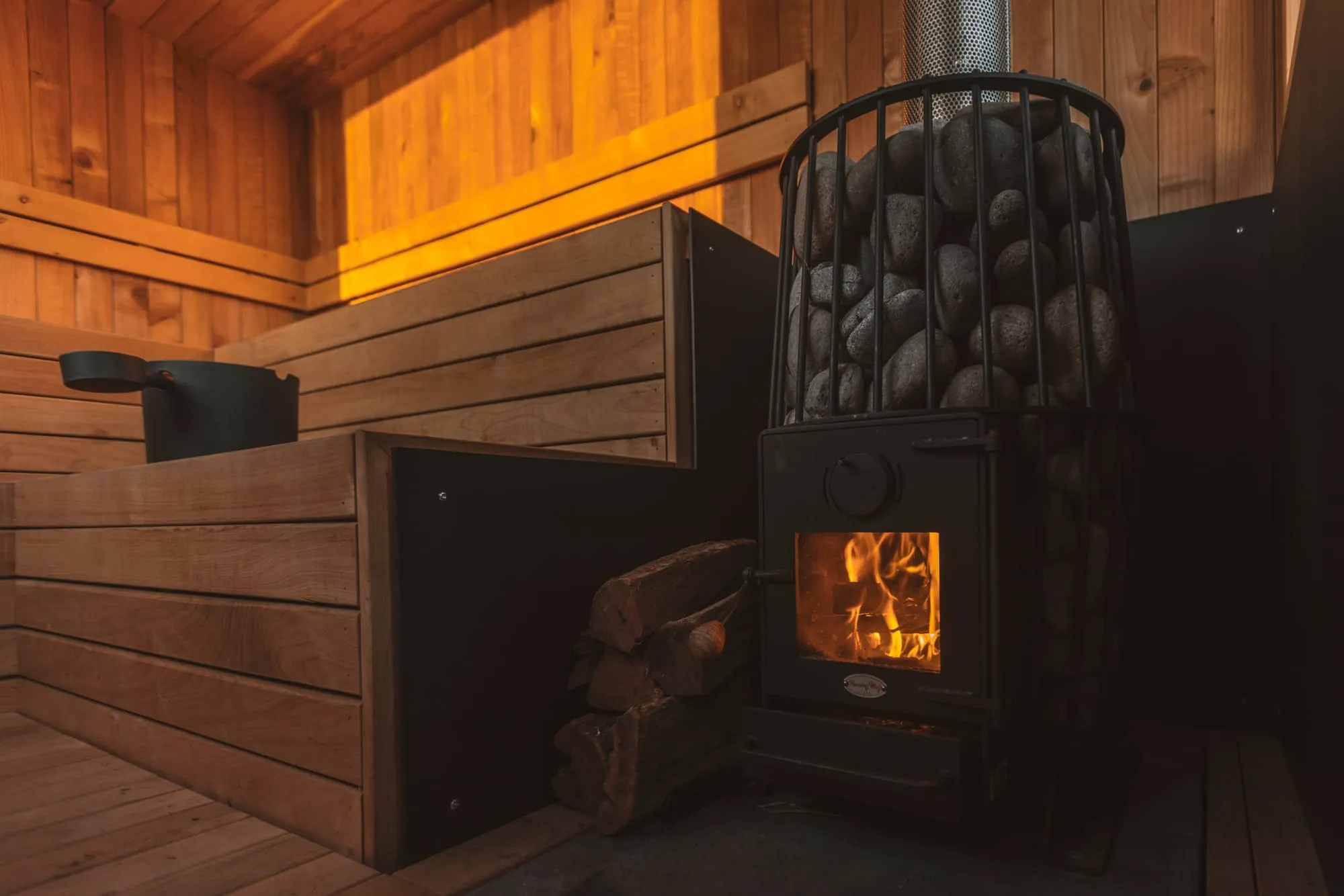 A wood-lined sauna interior with a wood-fired stove glowing